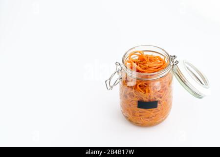 500 Gramm würziger koreanischer Karottensalat mit Öl, Knoblauch und schwarzem Pfeffer im Glasbecher. Nachhaltige Verpackung, weißer Hintergrund, hohe Auflösung Stockfoto