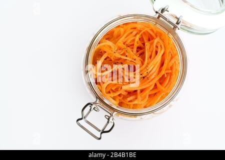 500 Gramm würziger koreanischer Karottensalat mit Öl, Knoblauch und schwarzem Pfeffer im Glasbecher. Nachhaltige Verpackung, weißer Hintergrund, hohe Auflösung Stockfoto