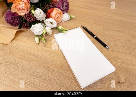 Wunderschöner Blumenstrauß aus Rosen auf Holzhintergrund, Notizbuch und Bleistift. Stockfoto