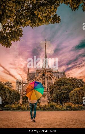 Junge Frau, die in Notre Dame Paris in Frankreich spazieren geht, Farben bei Sonnenuntergang Notre Dame Paris, Regenbogenschirm Stockfoto