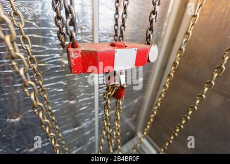 Metallischer Kettengriff mit rotem Haken im Technikraum. Kran-Frachthaken. Konzept der Wartungs- und Bauarbeiten. Stockfoto