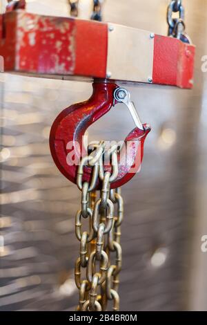 Metallischer Kettengriff mit rotem Haken im Technikraum. Kran-Frachthaken. Konzept der Wartungs- und Bauarbeiten. Stockfoto