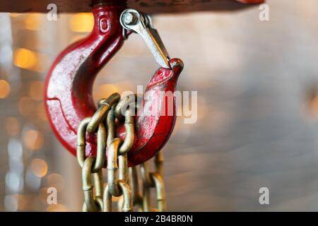 Metallischer Kettengriff mit rotem Haken im Technikraum. Kran-Frachthaken. Konzept der Wartungs- und Bauarbeiten. Stockfoto