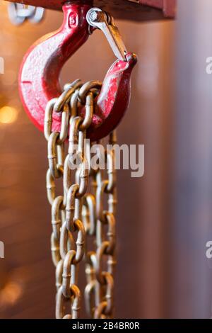 Metallischer Kettengriff mit rotem Haken im Technikraum. Kran-Frachthaken. Konzept der Wartungs- und Bauarbeiten. Stockfoto
