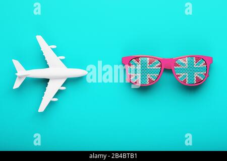 Rosafarbene Brille mit der Flagge Großbritanniens in Linsen auf blauem Hintergrund mit weißem Flugzeug. Reisen nach England. Freiheit und Gleichheit Stockfoto