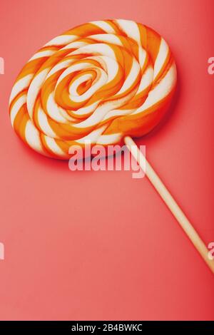 Orangefarbenes Lollipop auf pinkfarbenem Hintergrund mit weichem Kontrast. Minimales Konzept mit Kopierraum. Süßwaren und Süßigkeiten im Urlaub. Stockfoto