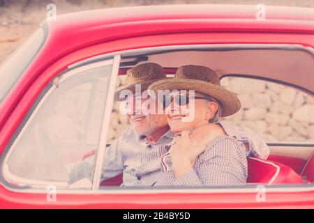 Schöne Erwachsene Paare umarmen und lieben in einem roten alten Oldtimer, der auf der Straße geparkt ist. Lächelt und viel Spaß beim gemeinsamen Reisen. Glück und Lebensstil für nette Leute. Sommerzeit und Urlaubsreise Stockfoto