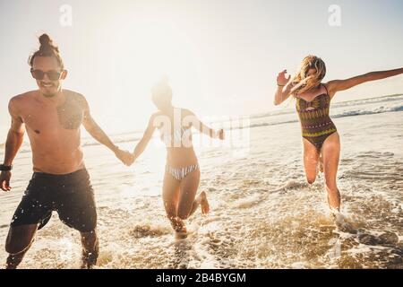 Eine Gruppe junger Leute, die mit Spaß den Sommerurlaub am Strand zum Wasser genießen, in spielerischer Freizeiterlebung zusammen - Jugendliche Männer und Frauen Stockfoto