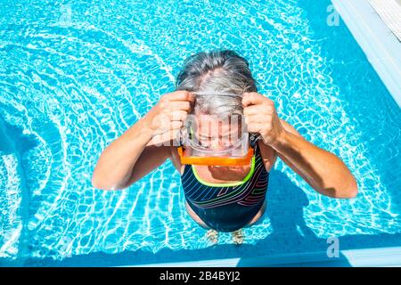 Silver Society alte aktive Frau nimmt Tauchmaske zum Schwimmen im Schwimmbad und genießt die Sommerzeit in klarem blauem Wasser - gesunder Lebensstil für Rentner im Freien Stockfoto