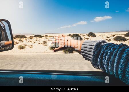 Menschen, die mit dem Auto und Sommerurlaub reisen - Frauenhandspiel mit dem Wind vor dem Fenster des Fahrzeugs, während sie auf einer Straße mit Wüstenhimmel und blauem Naturhimmel im Hintergrund fahren Stockfoto