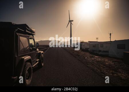 Lange Straße mit schwarzem Geländewagen 4x4 mit Zelt auf dem Dach - malerische Landschaft für Reiseabenteuer wildes Konzept und verschiedene Urlaubsdestination - Sonne und Sonnenlicht mit warmem Himmel Stockfoto