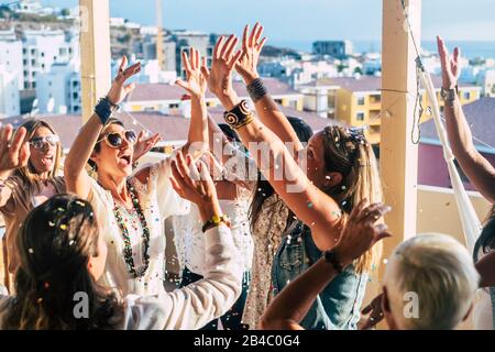 Gruppe glücklicher junger Menschen kaukasische Frauen mit ternder Mode feiern zusammen mit viel Spaß mit farbigen Konfetti und schöner landschaftlich schöner Aussicht auf die Stadt von der Dachterrasse - Glück und fröhliche Party Stockfoto