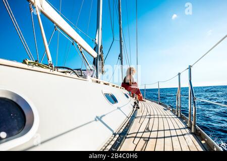 Fröhliche glückliche Leute, die eine Segelbootfahrt während der Freizeitreise im Freien und Sommerurlaub in Freiheit genießen - schöne Frau setzt sich hinab und spürt das blaue Meer Stockfoto