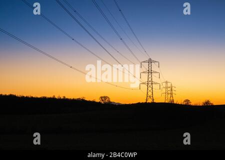 Ein Winteruntergang hinter Stromleitungen und Pylonen in Milton bei Brampton, Cumbria UK Stockfoto