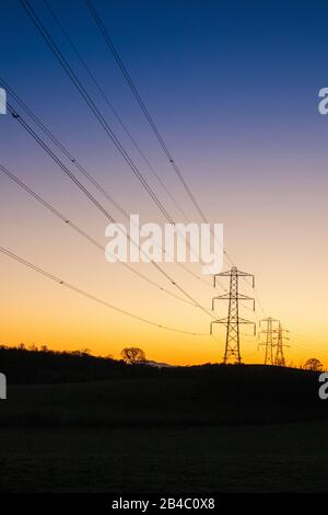 Ein Winteruntergang hinter Stromleitungen und Pylonen in Milton bei Brampton, Cumbria UK Stockfoto