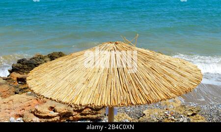 Isolierter einzelner Bambusparasol am Strand von Gouves auf Crete Stockfoto