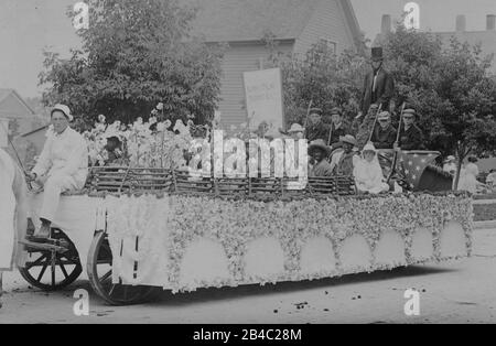 Rassistische Parade Wagen von Blackface und weißen Kindern sitzen in einem dicken Baumwollfeld auf einem Pritschenwagen, c.. 1915. Rund um das Feld und Kinder ist eine Imitation Split Rail Zaun. Andere Jungen, die als Soldaten mit Gewehren aus der Zeit des Bürgerkriegs bewaffnet sind, wachen über sie. Ein Mann, der als Präsident mit Kopfbeschlag gekleidet ist, Abe Lincoln steht in der Rückseite und hält ein gerolltes Papier. Hinter den Kindern und der Baumwolle ist ein hohes weißes Banner, schwach mit 'Lincoln School' gedruckt. All diese Leute und die Lage sind unbekannt. Um meine verwandten Vintage-Bilder zu sehen, Suche: Prestor vintage African Stockfoto