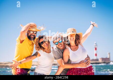 Eine Gruppe glücklicher Menschen und fröhlicher Erwachsener, die zusammen während des Sommerurlaubs am Strand Spaß haben - den Strand und das Meer im Freien genießen - blauer Himmel und Leuchtturm im Hintergrund Stockfoto