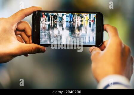 Nahaufnahme von Mann oder Frau, die ein Bild von den Beinen einer großen Gruppe von Menschen machen, die auf ihren Flug am Flughafen warten - und warten, bis sie an ihrem Tor oder an ihrem Eingang einsteigen Stockfoto