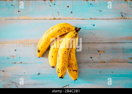 Nahaufnahme von gelben und marronfarbenen Bananen auf einem blauen Holztisch - Ernährung und gesunder und vegetarischer oder veganer Lebensstil - Kalium- und saisonales Lebensmittelkonzept in vertikaler Sicht Stockfoto