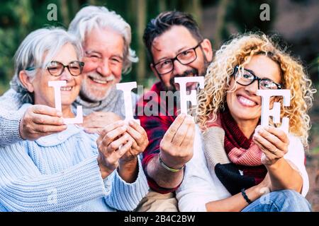 Eine Gruppe gemischter Generationen lächelt und zeigt Blockbriefe mit Lebenswort - fröhliche Lebensfreude, die gemeinsam wie eine Familie die Freizeitgestaltung im Freien genießen Stockfoto