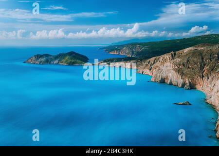 Blick auf die Stadt Assos und die Burgruine Frourio auf der Spitze. Schöne, milchige blaue Bucht mit brauner Kalksteinkuste und beweglichen weißen Wolken am Horizont, Insel Kefalonia, Griechenland. Stockfoto