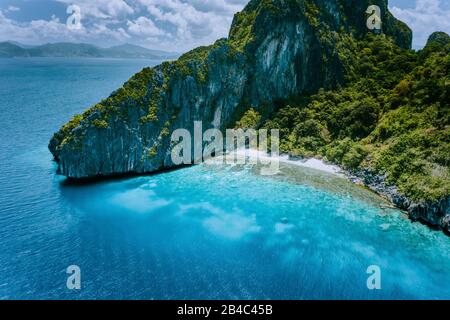 Luftdronblick auf die tropische Entalula-Insel. Riesige Steilfelsen Klippen Berge rund um die blaue Bucht mit wunderschönem Korallenriffe. Insel-Hopping-Tour El Nido, Palawan. Stockfoto