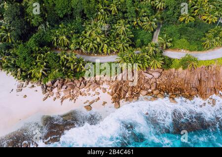 Seychelles Mahe Island Luftdrone Landschaft der Küste. Entlang der Küste des paradiesischen Sandstrands mit Palmen und blauen Meereswellen, die gegen Granit-Felsen rollen. Stockfoto