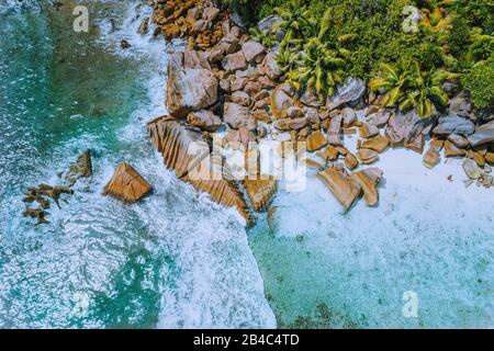 Anse Cocos Strand tropische Insel La Digue Seychellen. Drohnenansicht der Schaum-Ozeanwellen, die auf die felsige Küste und Palmen zurollen. Stockfoto