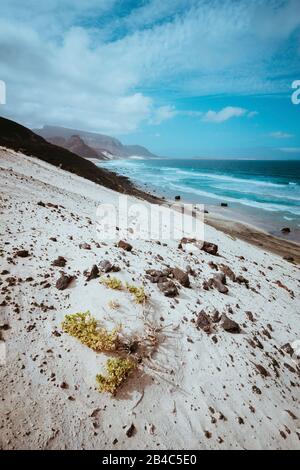 Abgelegener Strand Praia Grande. Spektakuläre Sanddünen, Meereswellen und schwarze Vulkansteine. Karges Vegetaion von Calhau, Insel Sao Vicente Kap Verde. Stockfoto