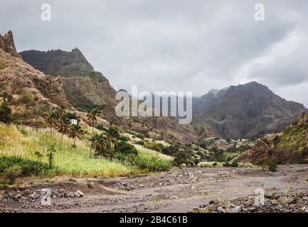 Panorama des ausgetrockneten Baches, umgeben von fruchtbarem grünen Tal und zerklüfteten Klippen. Einsame weiße Behausung auf dem Hügel. Santo Antao, Cabo Verde. Stockfoto