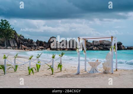 Hochzeitsfeier des Strandbogens mit weißen Blumen an einem tropischen weißen Sandstrand. Exotische Hochzeit im Paradies. La Digue, Seychellen. Stockfoto