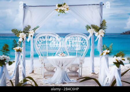 Hochzeitsbogen mit Gartenlaube, dekoriert mit weißen Blumen an einem tropischen großen strand von anse. Hochzeitssetup am Strand im Freien. La Digue, Seychellen. Stockfoto