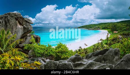 Malerischer Panoramaschuss von Grand Anse, La Digue Insel, Seychellen. Riesige Felsformation aus Granit, strahlend weißer tropischer Strand mit türkisblauem kristallklarem Wasser und Wolkenscape. Eden auf Erden Stockfoto