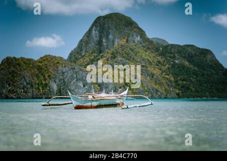 Traditionelles filippino banca Boot in der blauen tropischen Lagune an der El Nido-Bucht. Eindrucksvolle Karstberge von Cadlao Island in verschwommenem Hintergrund. Palawan Island, Philippinen. Stockfoto