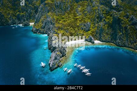 El Nido, Palawan, Philippinen. Luftansicht der Insel Miniloc mit Tauchbooten über Korallenriffen, umgeben von zerklüfteten Gebirgsklippen aus Karstkalk. Stockfoto