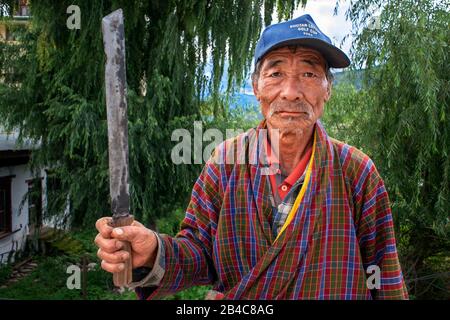 Porträt eines Bauern mit einem Messer im Paro Valley mit Reisfeldern, Die Tiere in der Nähe des Paro Chhu River Bhutan Bewirtschaften. Stockfoto