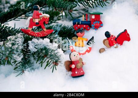Bunte traditionelle Weihnachtsbaumdekorationen aus Holz, die auf einem verschneiten Tannenzweig angeordnet sind Stockfoto