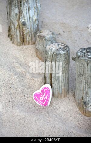 Rosafarbenes Steinherz mit Wortliebe an verwitterten Holzpfosten an einem sandigen Strand angelehnt Stockfoto