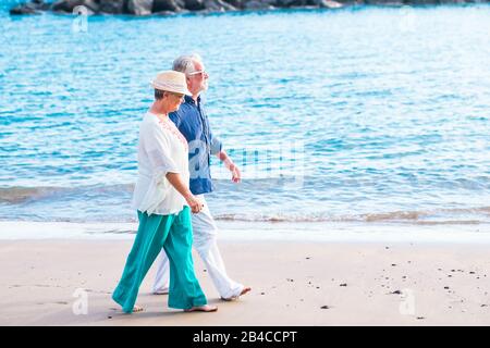 Ein paar Senioren, die am Strand auf dem Sand mit dem Meer im Hintergrund laufen - glückliche, reife Menschen haben mit einem netten, Reisenden Lebensstil geheiratet, der den Urlaub im Ruhestand genossen hat Stockfoto