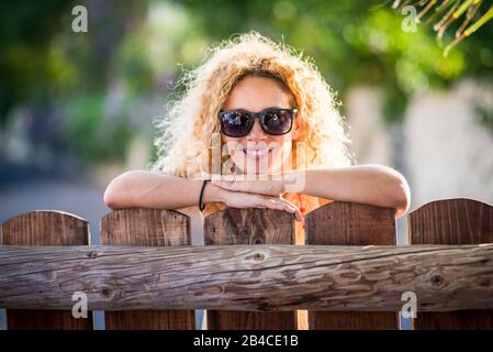Porträt einer schönen fröhlichen fröhlichen Frau mit Sonne in Hintergrundbeleuchtung und einem schönen Lächeln mit Blick auf die Kamera - grüner Naturhintergrund - genießen Sie die Freizeitgestaltung im Freien auf dem Land Stockfoto