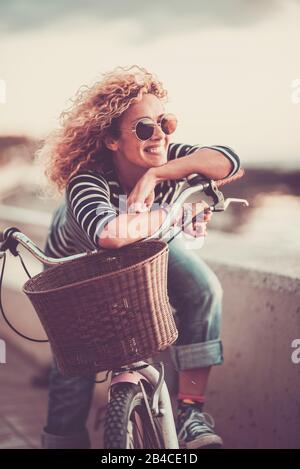Fröhliche, trendige junge, Erwachsene kaukasische Frau, die auf einem Fahrrad sitzt und lächelt - wunderschönes Frauenporträt - Konzept der Freizeitgestaltung im Freien und des Glücks und des fröhlichen Lebensstils Stockfoto