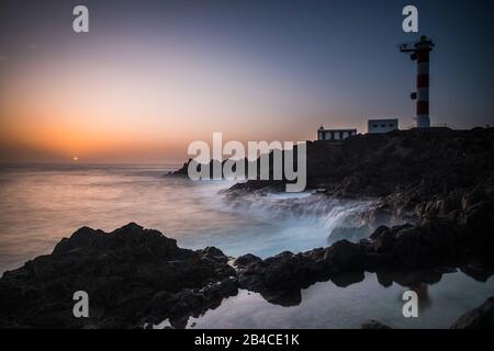 Wunderschöne Meeresozeanlandschaft mit großen Wellen auf den Felsen bei Sonnenuntergang mit klassischem Leuchtturm im Hintergrund - Reisekonzept und malerischer Ort Stockfoto