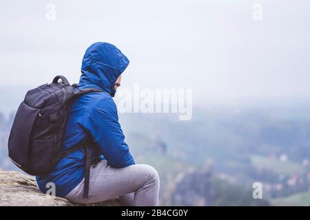 Wanderer mit Rucksack sitzen auf einem Felsen und genießt die Aussicht ins Tal, Reiseabenteuerl-Harmoniekonzept Stockfoto