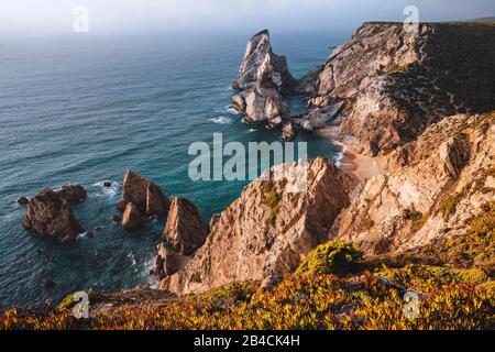 Strand Praia da Ursa mit Felsen im Vordergrund, die von Licht bei Sonnenuntergang beleuchtet werden. Surreale Landschaft von Sintra, Portugal. Küstenlandschaft am Atlantik. Stockfoto