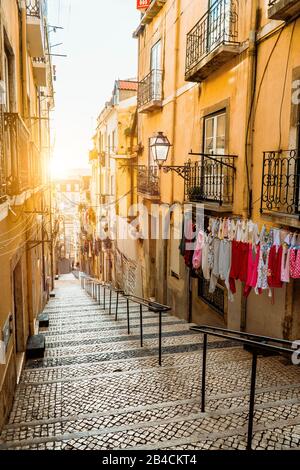 Treppenhaus in der Kopfsteinpflasterstraße in Lissabon. Hängende Wäsche in der typischen schmalen Straße. Sonnenuntergang in der Altstadt von Lissabon, Eindrücke von der Stadt. Lissabon. Stockfoto