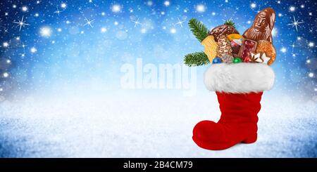 Red ST nicholas Day Stiefel gefüllt mit Schokolade weihnachtsmann Plätzchen Lebkuchen Zimtsterne orange und grüne frische Tannenzweige auf blauweißem Schnee p Stockfoto