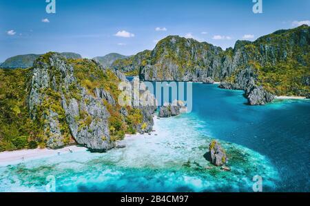 El Nido, Palawan, Philippinen. Blick auf die tropische Insel mit Touristenbooten, die am weißen Sandstrand vergraben sind. Jugged Karst Kalksteinmeerstapel Bergkuppen. Bacuit Archipel. Stockfoto