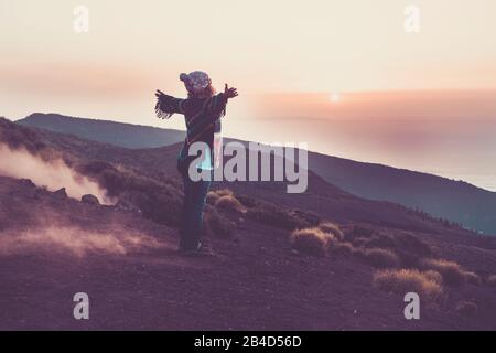 Glückliche Reisende Frau, die von den nach hinten öffnenden Armen aus gesehen wurde, um die wundervolle Natur während des Sonnenuntergangs zu umarmen - die Welt zu genießen und Menschen mit wanderlust leben - farbige Jacke - glückliche Reise-Leute in den Bergen Stockfoto