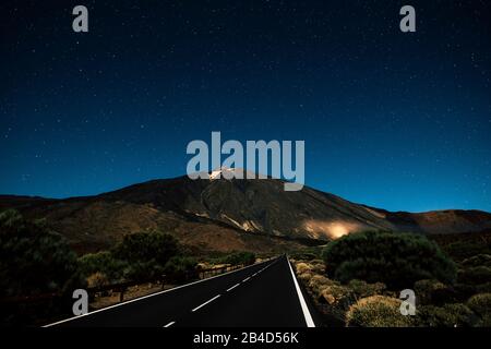 Lange gerade asphaltierte schwarze Straße bei Nacht mit Sternenhimmel oben - Reisekonzept und entdecken Sie die Schönheit der Welt - el teide vulkan-nationalpark teneras Stockfoto